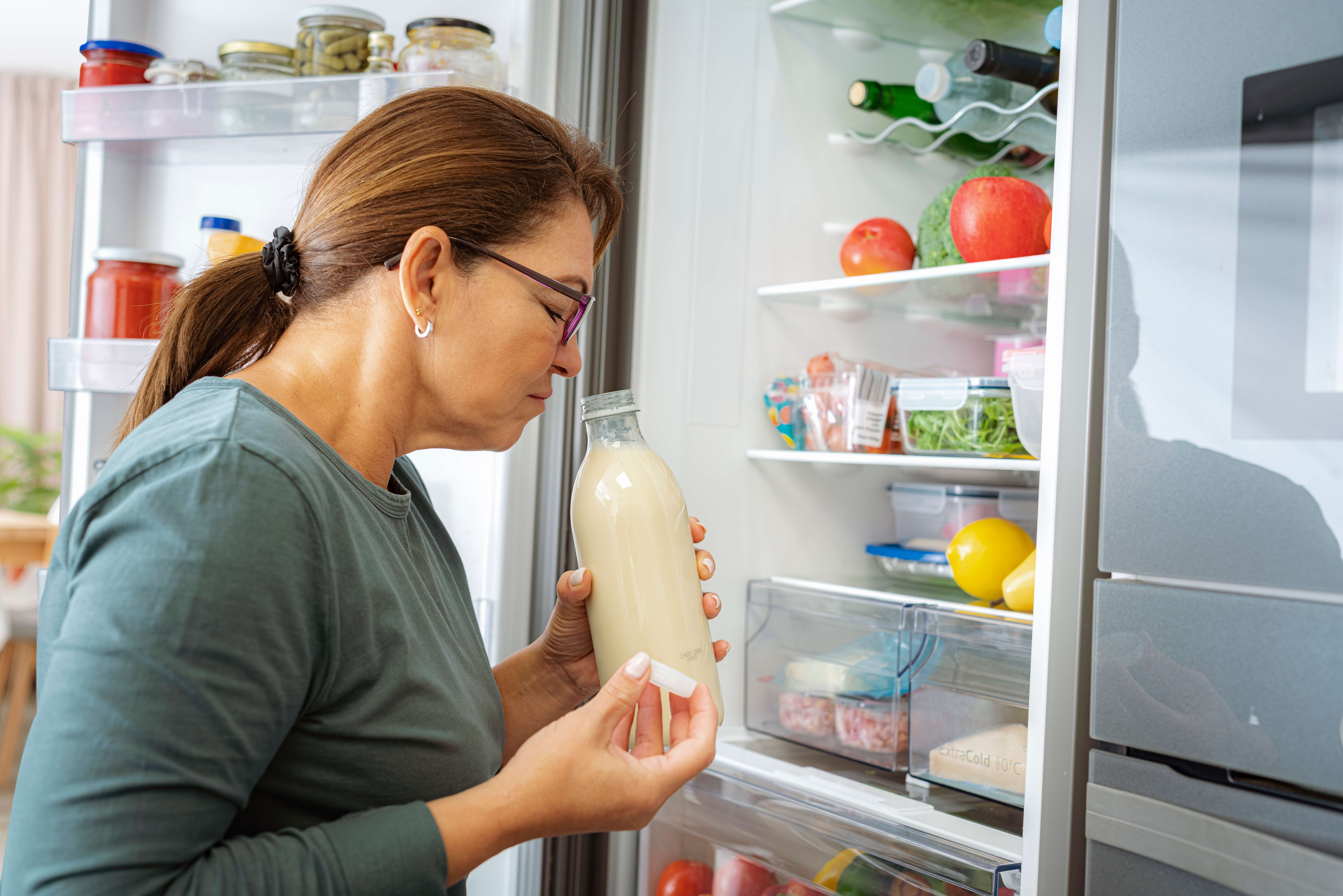 A senior woman smelling a milk bottle from the refrigerator
