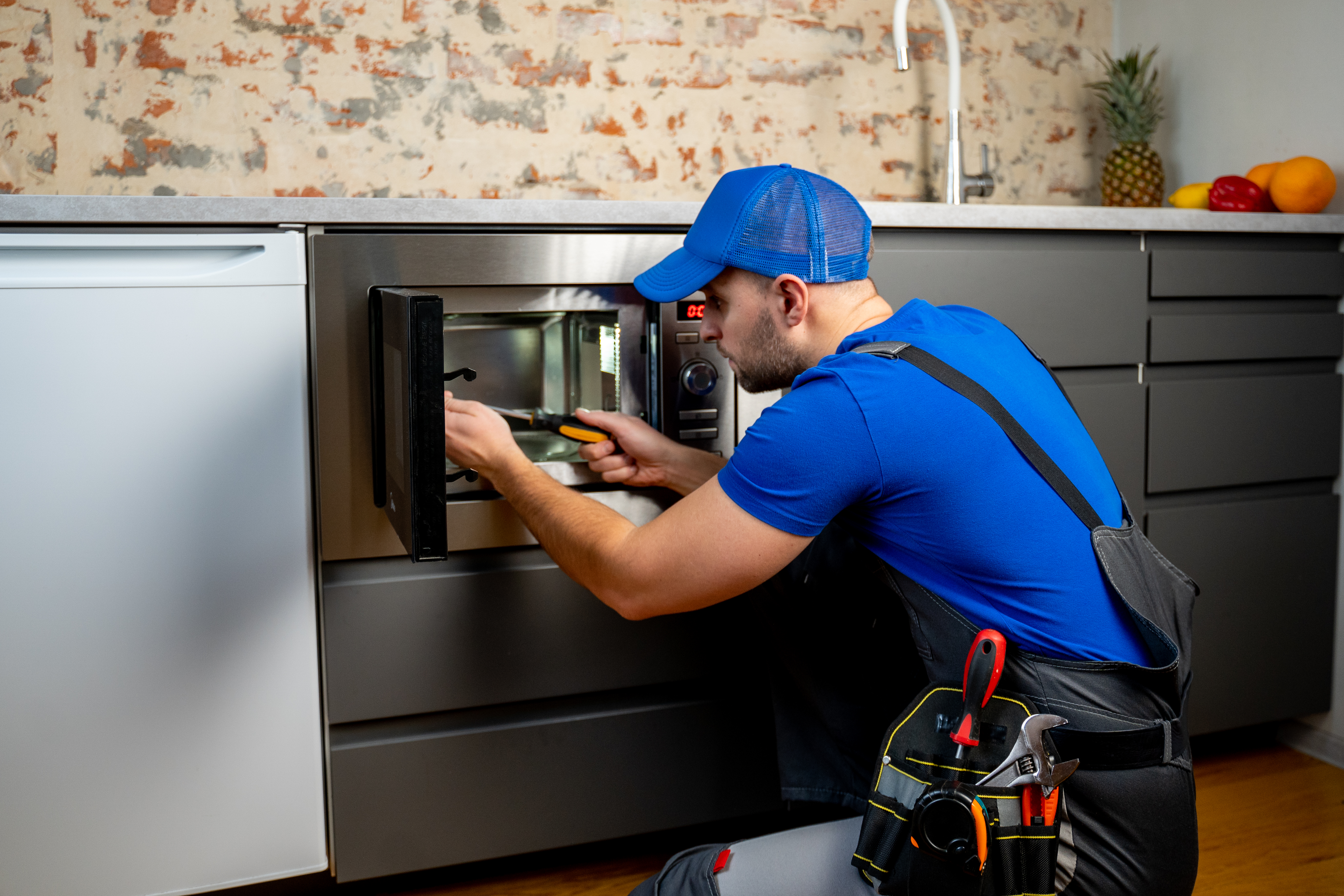 Technician in blue uniform repairing a microwave oven with a screwdriver, focusing on restoring the appliance's functionality.