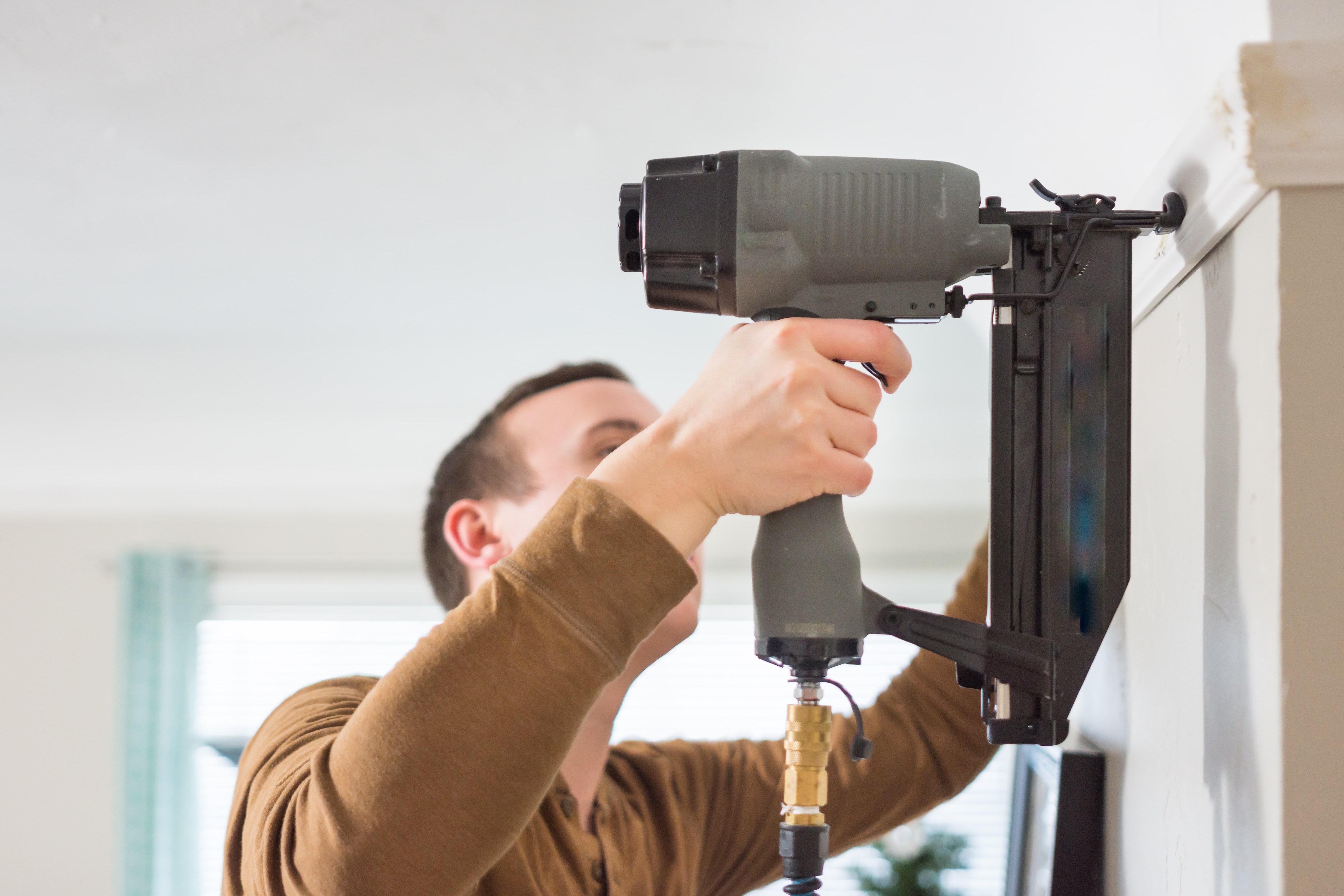 Man affixing crown molding to wall using brad nailer