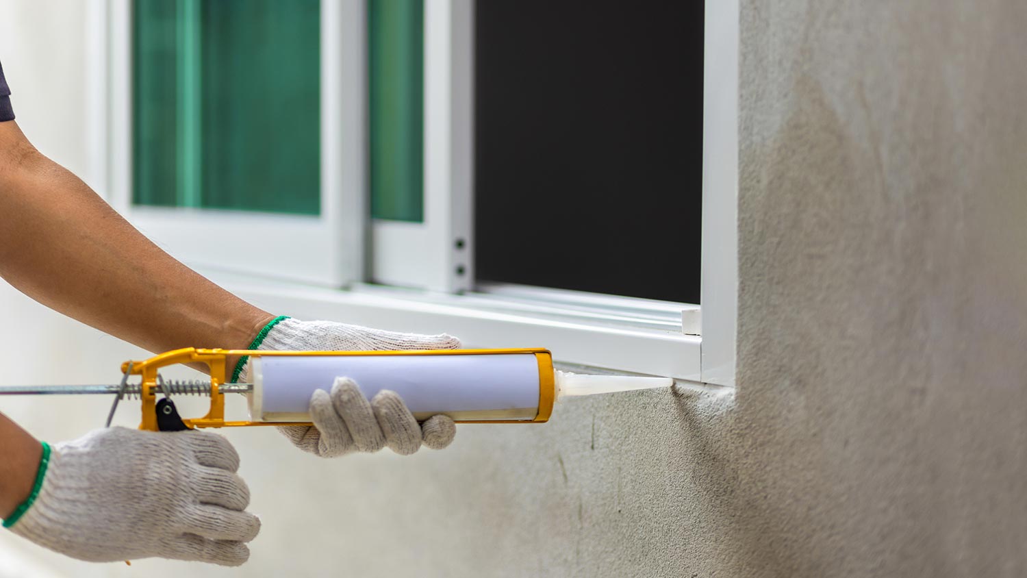 A person caulking the exterior of a window