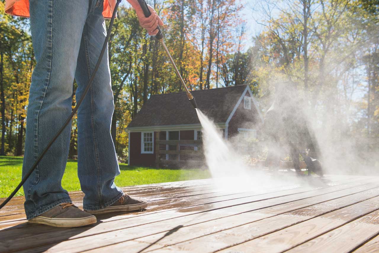 Worker using pressure washer machine to clean a deck